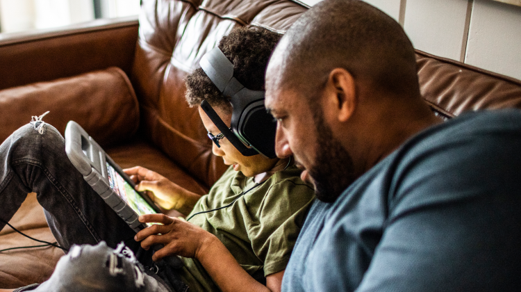 Dad and son sitting on their couch and browsing tablet, with Brightspeed fiber internet.