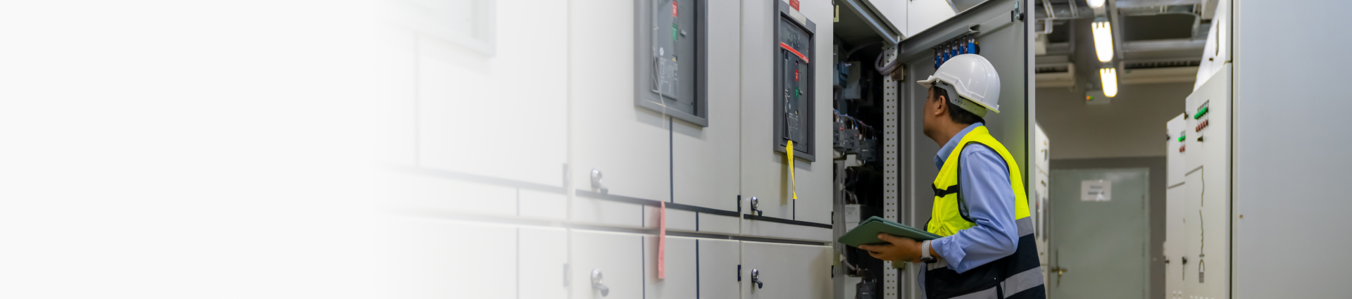 A technician inspects an electrical panel with a tablet in an industrial setting.